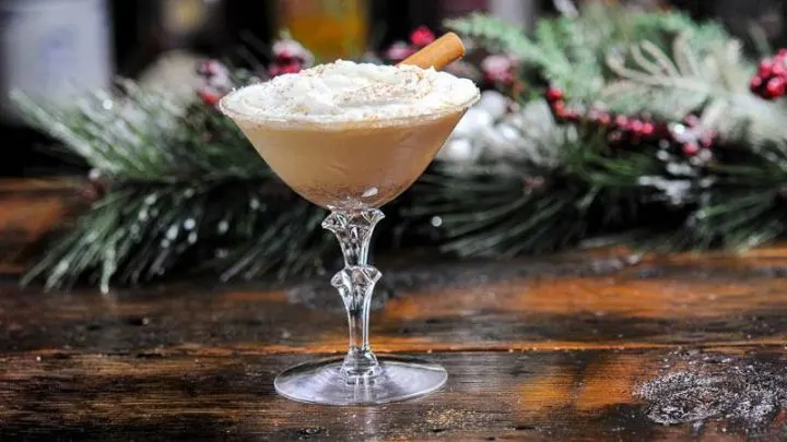 Tan cocktail in coupe with whipped cream and cinnamon roll