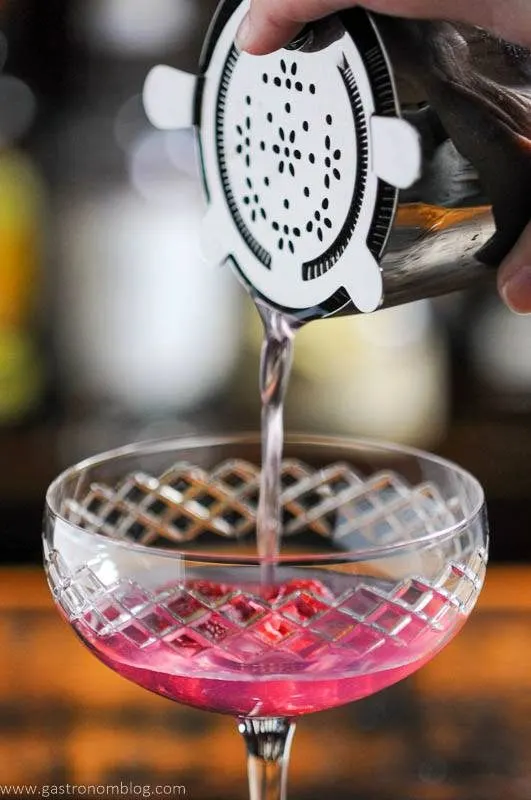 Pink cocktail being poured into coupe