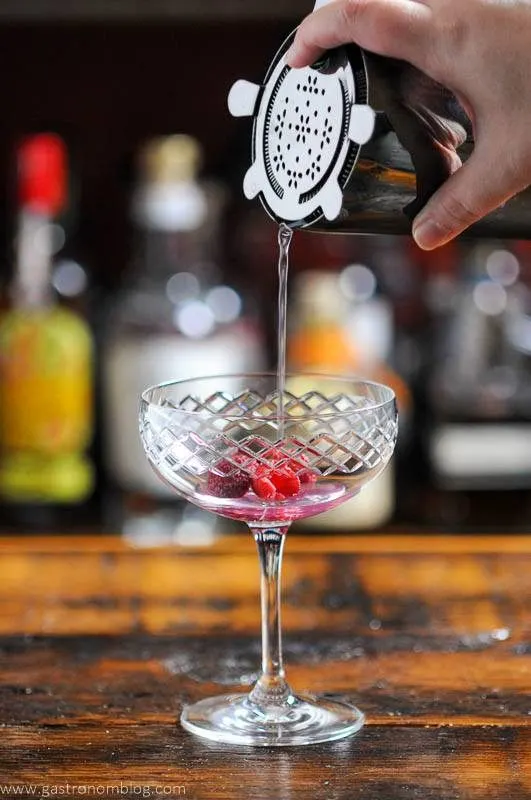 Pink cocktail being poured in coupe