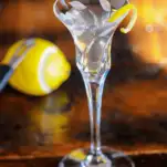 Clear cocktail in glass with lemon peel. Lemon in back with channel knife.