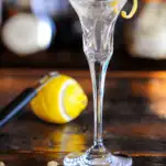 Clear cocktail in tall glass with lemon peel