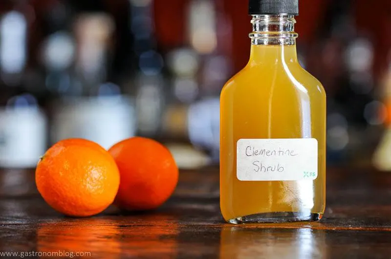 orange drinking vinegar in bottle, 2 oranges behind on wooden surface