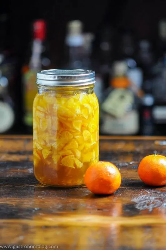 Orange shrub liquid in mason jar with 2 oranges on wooden surface