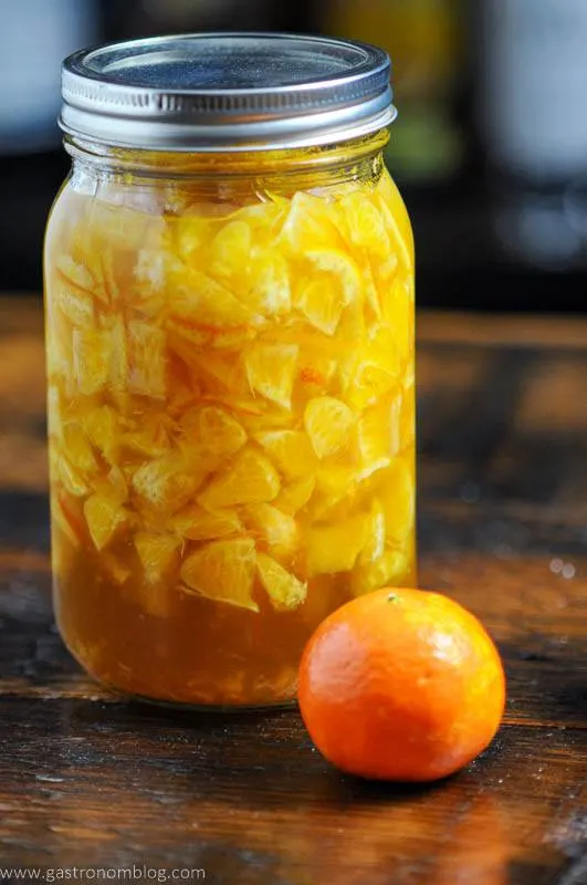 Clementine Shrub, or drinking vinegar, orange liquid in mason jar with an orange on wooden surface