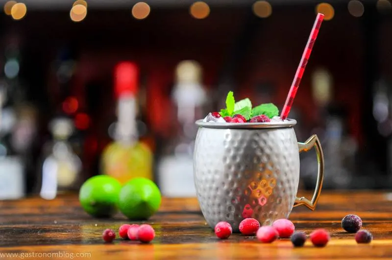 Cranberry drink in silver mug, cranberries, mint, black/red straw, limes in background