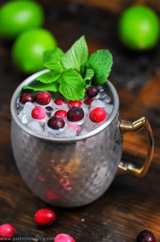 Cranberry drink in silver mug, cranberries, mint. Limes in background