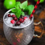 Mocktail in silver mug, cranberries, mint, and black/red straw, limes in background