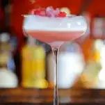 Pink cocktail in coupe with foam, dry ice and raspberries
