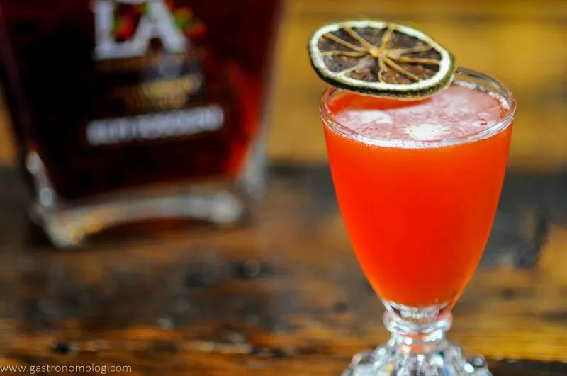 Pink cocktail in glass with citrus slice, liqueur bottle in background