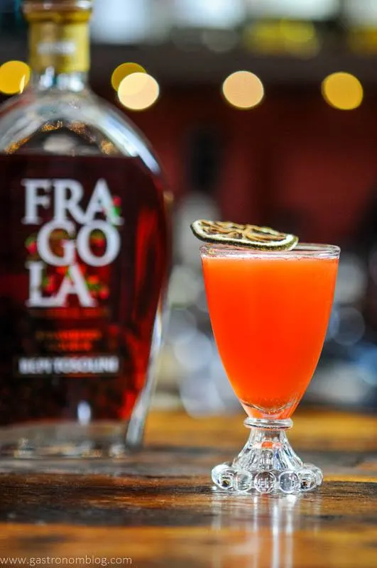 Strawberry cocktail in glass with citrus slice, liqueur bottle behind