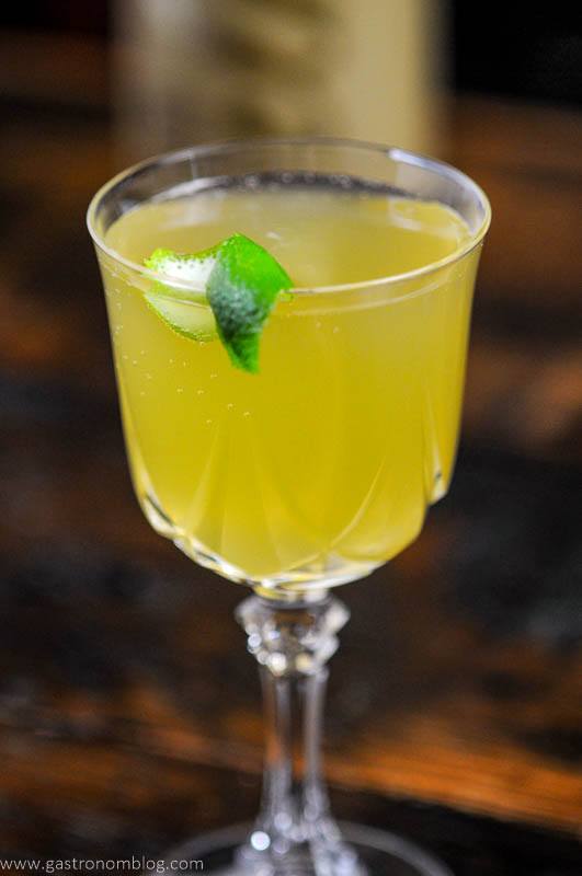 Yellow cocktail in glass, lime peel