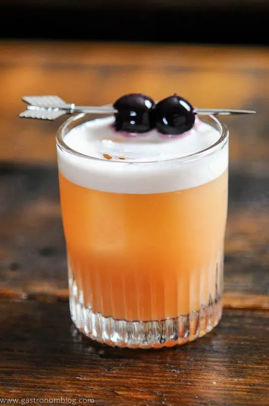 Peach colored cocktail with white foam, cherries