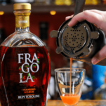 Strawberry Liqueur cocktail being poured into glass, liqueur bottle behind