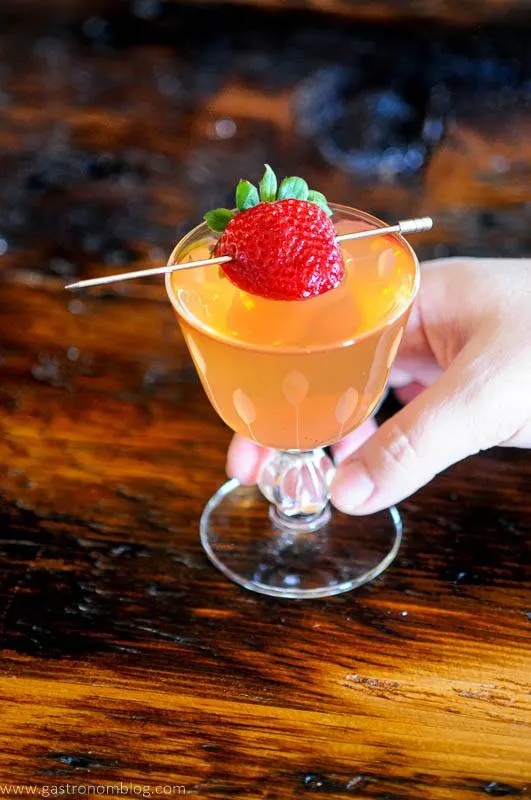 Pink cocktail in glass, strawberry on pick, hand holding glass