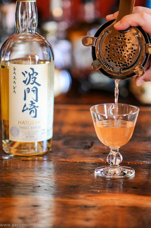Pink cocktail being poured into glass, Japanese whisky bottle in background