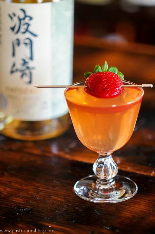 Pink cocktail, with berry on pick, Japanese whisky bottle in background