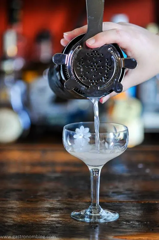 Pink Rhubarb Gimlet cocktail being poured into a coupe from a shaker.