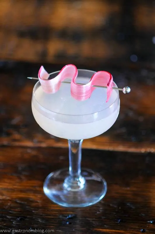 Pink cocktail in coupe with rhubarb garnish on pick
