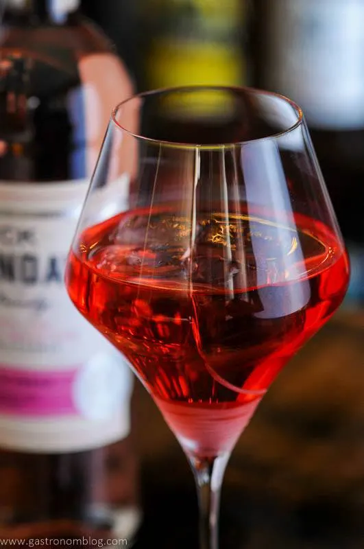 Pink cocktail in wineglass with wine bottle behind