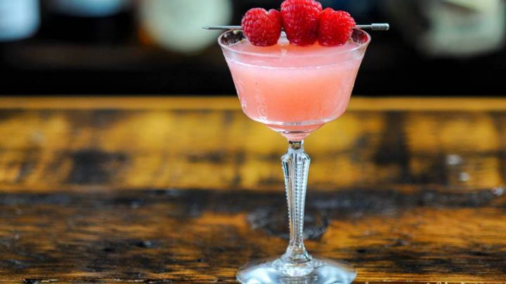 Raspberry Gimlet cocktail, pink cocktail in coupe with raspberries on cocktail pick