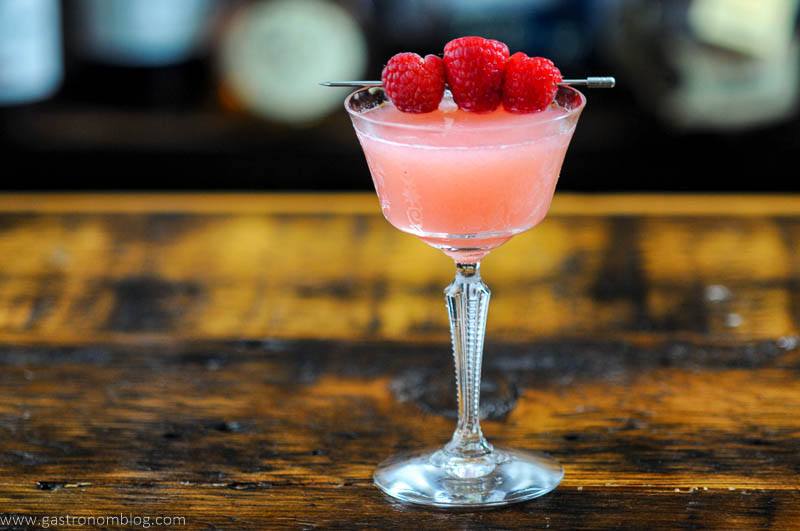 Raspberry Gimlet cocktail, pink cocktail in coupe with raspberries on cocktail pick