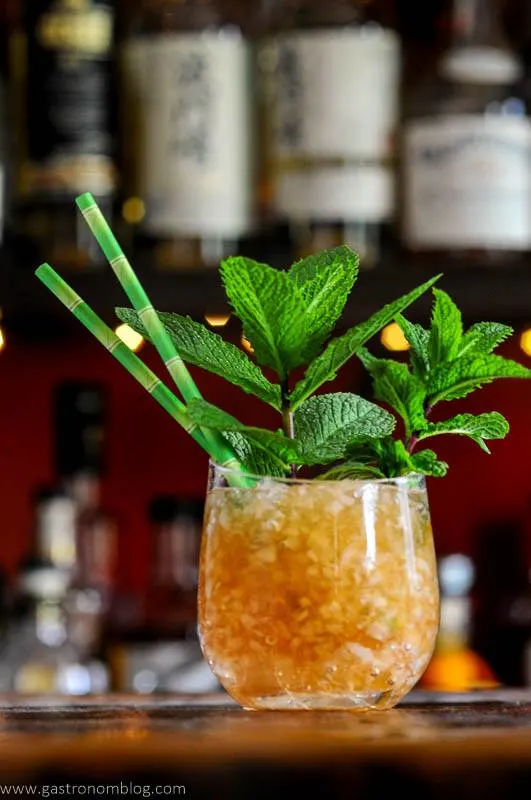 tan cocktail in glass with crushed ice, mint bunches and green straws