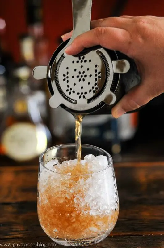 Tan cocktail being poured from shaker into glass wtih crushed ice