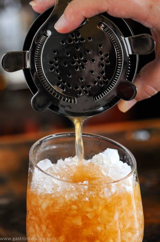 Tan cocktail being poured into glass with crushed ice from shaker