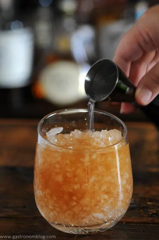Navy Grog cocktail in glass with crushed ice, club soda being poured out of jigger
