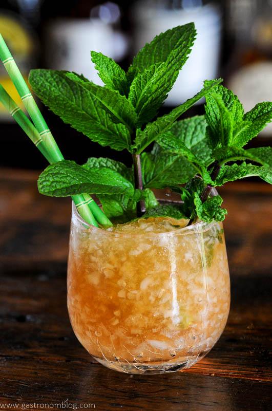 Tan cocktail in glass with crushed ice, mint bunches and straws