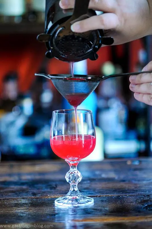 Hot pink cocktail being double strained with 2 strainers into cocktail glass