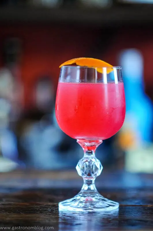 Bright pink cocktail in glass wtih orange peel
