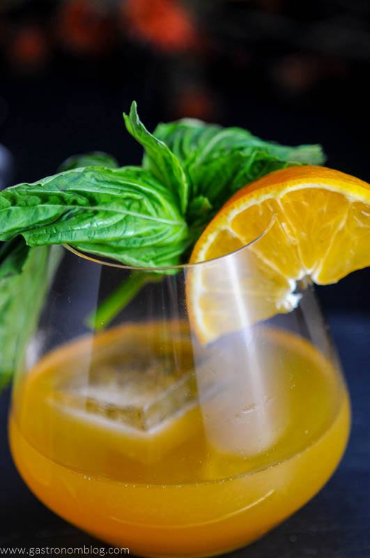 Orange cocktail in glass with orange slice and basil bunch