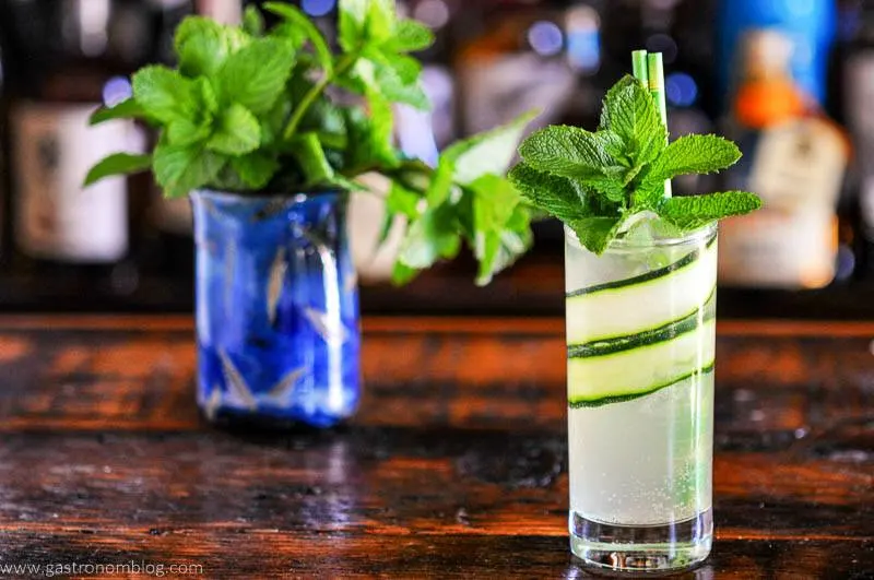 tall glass lined with cuucmber slices, mint garnish, blue glass behind filled with mint
