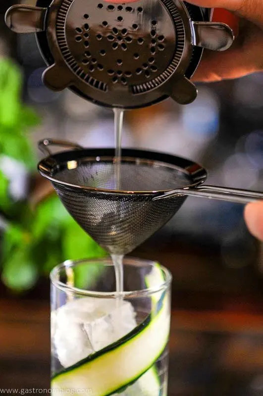 Cocktail being double strained into glass with clear ice