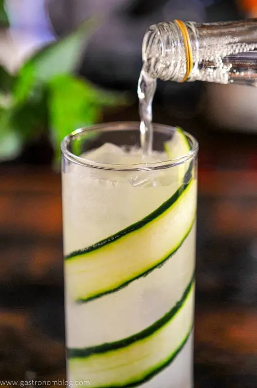 Tonic being poured into glass lined by cucumber slices