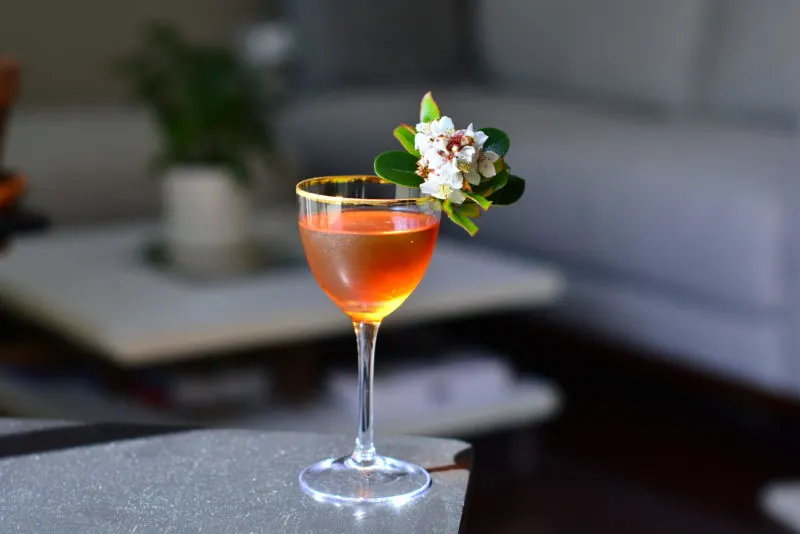 Tan cocktail in glass with white flower garnish