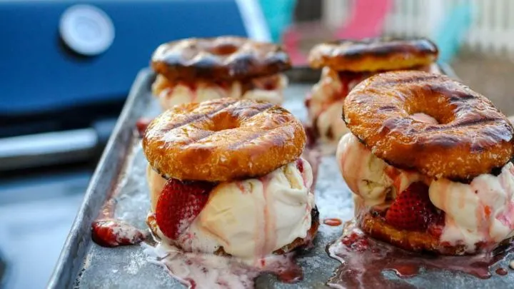Grilled doughnuts filled with ice cream on cookie sheet in front of blue grill
