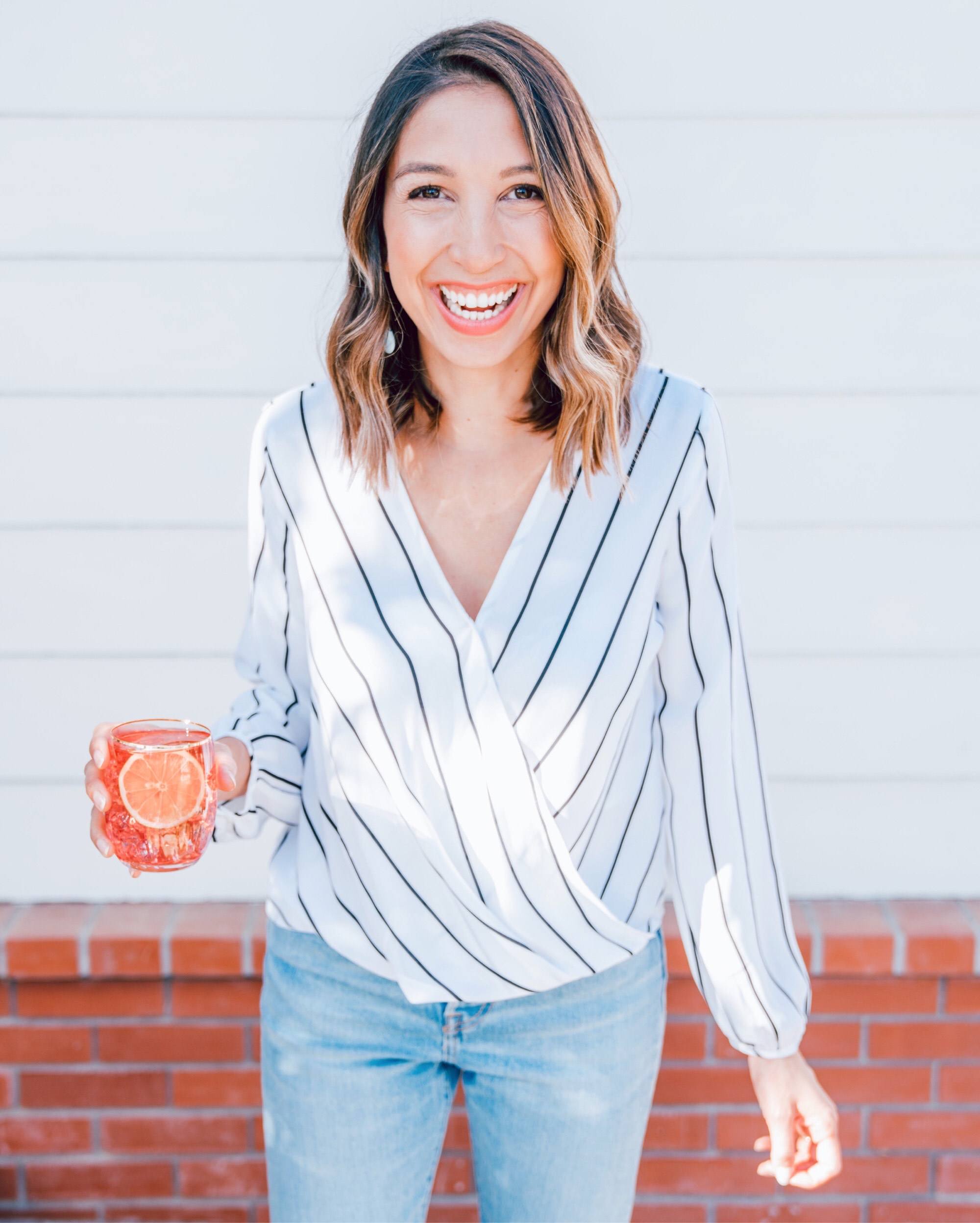 Woman in striped shirt and jeans, smiling and holding a cocktail