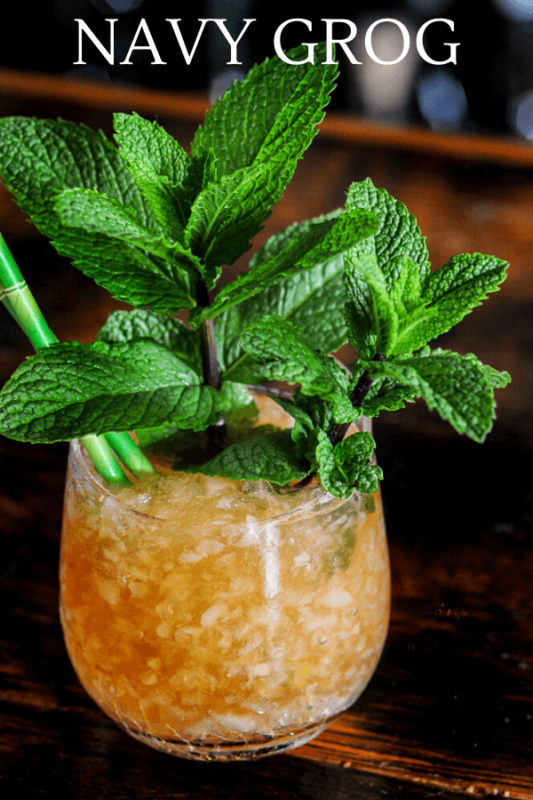Tan cocktail in glass with crushed ice, mint bunches and green straws