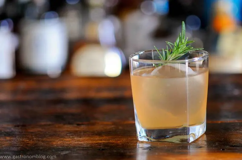 light orange cocktail in glass with ice and rosemary sprig