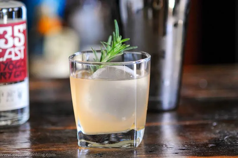 light orange cocktail in glass with rosemary, shaker behind