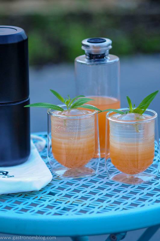Orange cocktail in 2 glasses and a decanter outside on a blue table