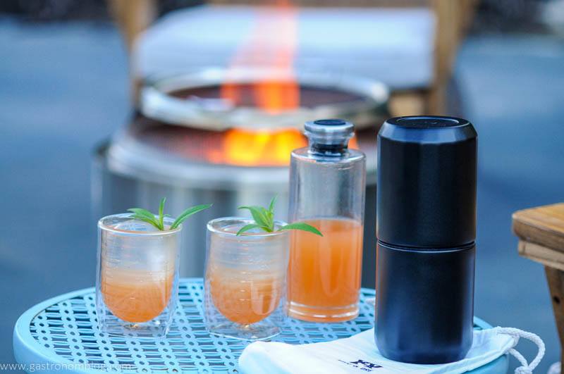 Orange cocktail in 2 glasses and a decanter outside on a blue table