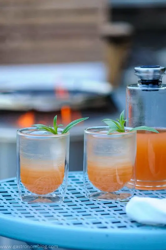 Orange cocktail in 2 glasses and a decanter outside on a blue table