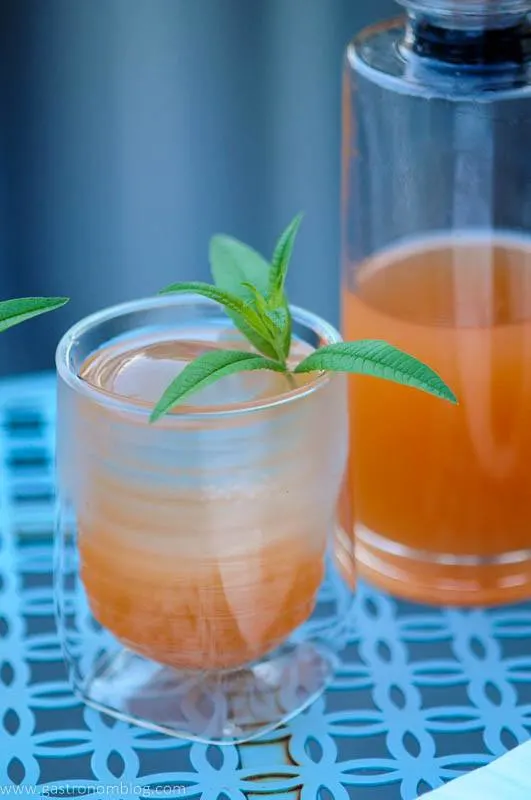 Rum Punch Cocktail is in a glass and a decanter. Lemon verbena garnish