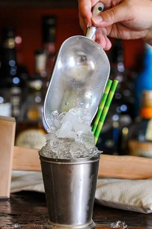 Ice being poured into a silver cup with a scoop, green straws