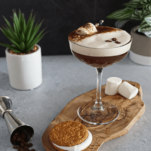 Brown cocktail with white foam, dessert and bottle behind