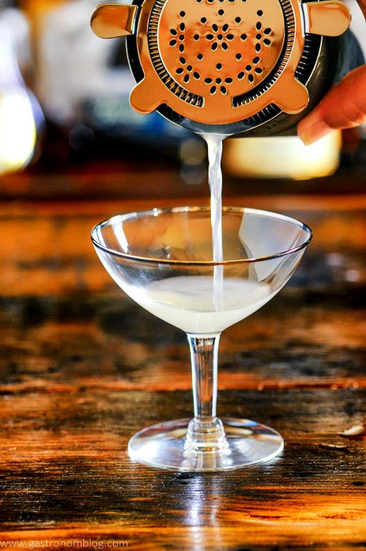 opaque cocktail being poured into coupe