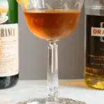 Brown cocktail in coupe, alcohol bottles behind